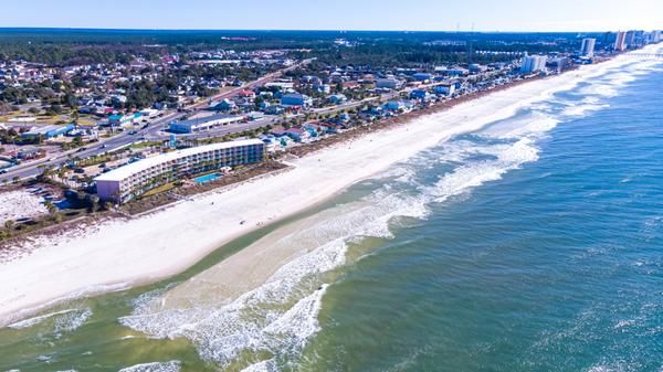 Aerial view of a beachfront town with colorful buildings along a long white-sand beach and blue ocean.